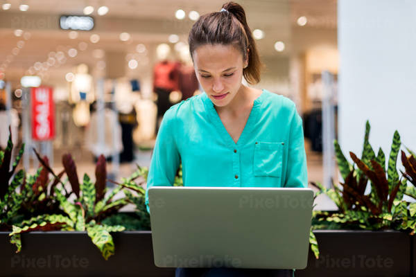 Young Woman Working on a Laptop Remotely in a Shopping Mall