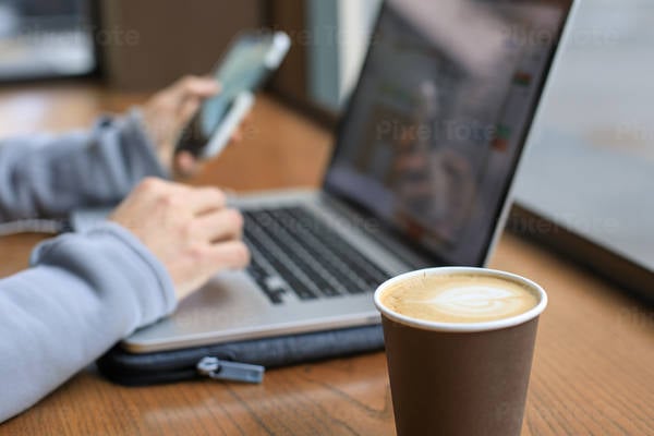 Man Working on a Laptop in Cafe While Holding His Phone