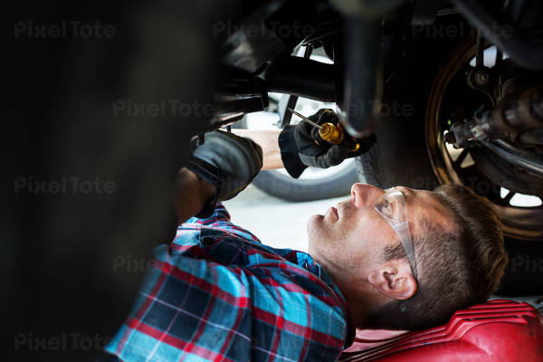Male Auto Mechanic Laying on a Creeper Working Underneath the Front of a Car