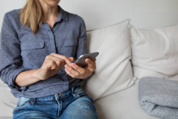 Young Woman Sitting on a Sofa at Home Using a Smartphone