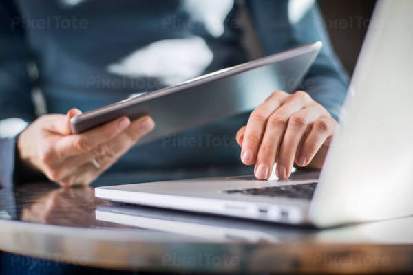 Low-Angle View of a Woman Holding a Digital Tablet While Typing on a Laptop Keyboard