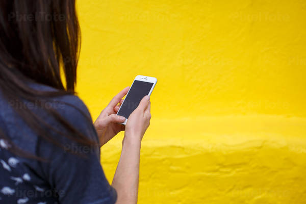 Over-the-Shoulder View of a Woman on a Cell Phone with a Yellow Wall Behind
