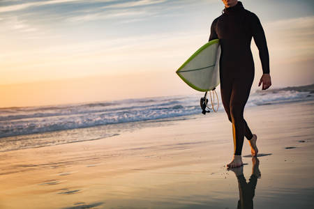 Male Surfer with a Surfboard Walking on a Beach During Sunset