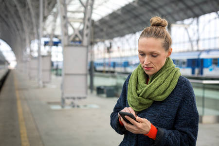 Woman with a Smartphone on a Train Station Platform