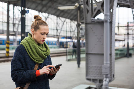 Woman with a Smartphone Standing on a Train Station Platform