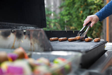 Man Placing Sausages on a Barbecue in a Garden