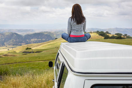 Girl Sitting on the Roof of a VW Bus Looking at Rolling Hills in the Distance