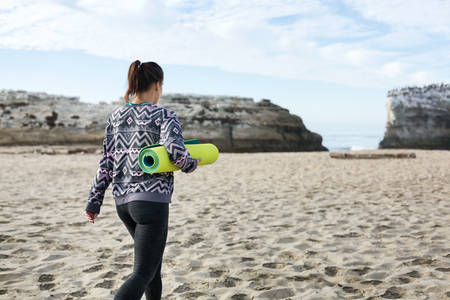 Young Woman with a Yoga Mat Walking on a Sandy Beach