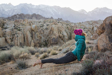 Woman in a Down Jacket Practicing Yoga in a Rocky Terrain