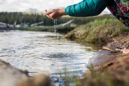 Woman Scooping Fresh Water from a Mountain Creek 