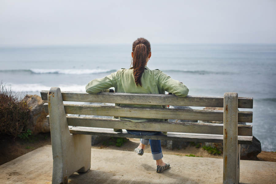 Rear View of a Woman Sitting on a Bench on a Coast Stock Photo — PixelTote