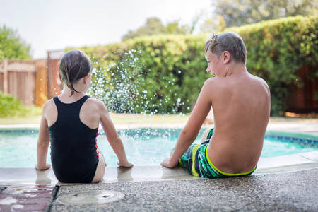 Two Children Sitting on a Side of an Outdoor Pool