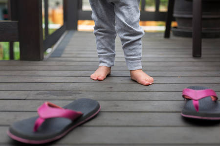 Toddler Girl Standing Next to Pink Flip-Flops on a Porch