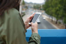 Woman Using a Cell Phone Standing on a Bridge with a Road Below Woman Using a Cell Phone Standing on a Bridge with a Road Below