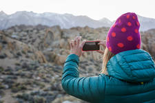 Woman in a Beanie Taking a Picture of Mountains with a Smartphone