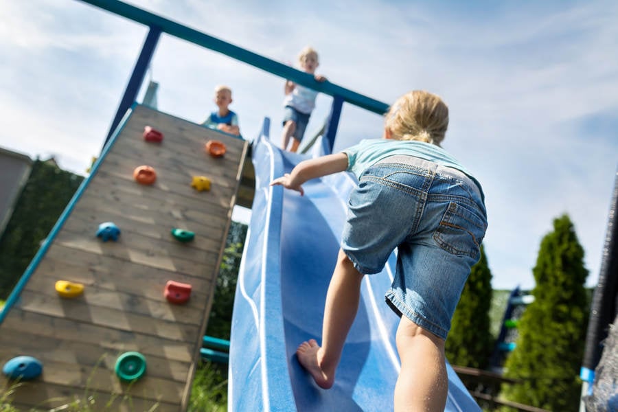  Three children are playing on a playground. One child is climbing up the slide while another is sliding down. A third child is climbing on top of the structure.