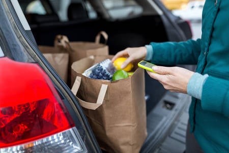 Woman Using a Cell Phone and Arranging Groceries in a Hatchback Car