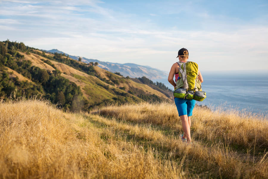 Woman with a Backpack Hiking Stock Photo - Th Ls Lg Woman With A Backpack Hiking On A Trail With A View Of An Ocean Default Stock Photo