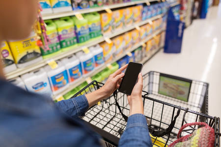 Woman Shopping for Groceries Using a Cell Phone While Pushing a Shopping Cart