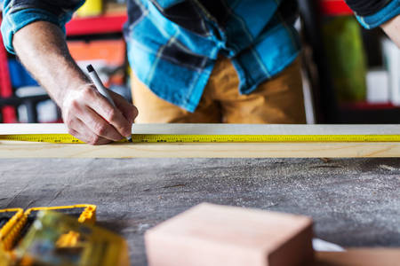 Handyman Using a Measuring Tape for a Woodworking Project in a Workshop