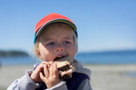 Toddler Girl Taking a Bite from Sandwich on a Beach