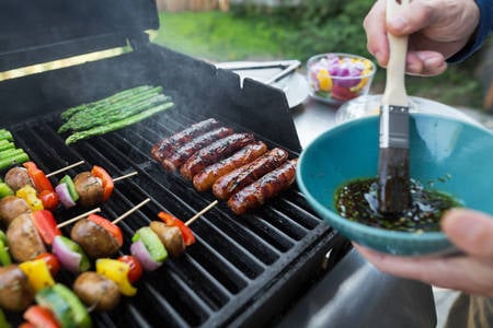 Man Braising Sausages on a BBQ Grill in a backyard
