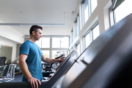 Man Selecting a Running Workout Setting on a Treadmill in a Gym