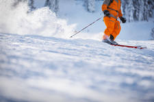 Downhill Skier in an Orange Outfit Going Through Fresh Powder