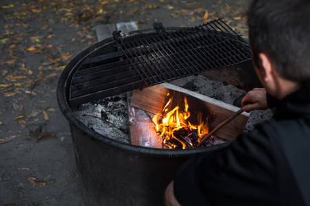 View of a Man Starting a Fire in a Fire Pit in Campground