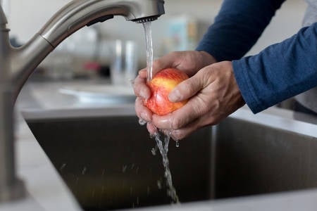 Man's Hands Rinsing an Apple under Kitchen Faucet
