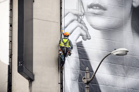 Worker Climbing a Rope While Installing an Outdoor Advertising Banner