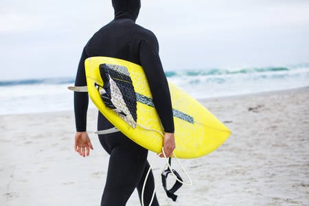 Male Surfer in a Wetsuit Walking on a Beach Carrying Surfboard