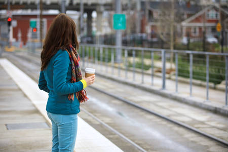 Woman Holding a Cup of Coffee Waiting for a Train at a Public Transportation Platform