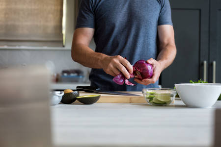 Man Peeling an Onion on a Cutting Board in a Kitchen
