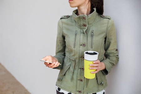 Woman Standing by a Wall Holding a Cell Phone and a Coffee Mug