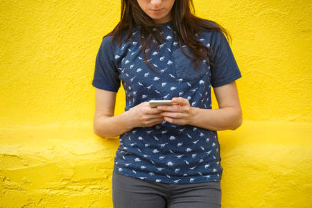 Woman Looking at Her Phone in Front of a Yellow Wall