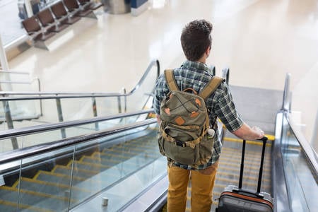 Traveler with a Backpack and a Luggage Standing on an Escalator at an Airport Lobby