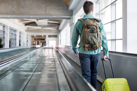 Traveler with a Luggage Walking on a Moving Walkway at an Airport Corridor