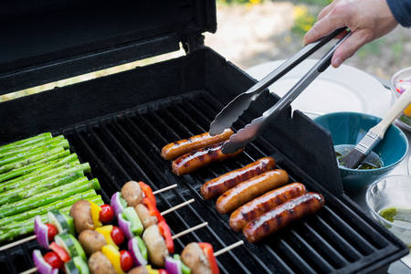 Man Arranging Sausages on a BBQ Grill with Kitchen Tongs