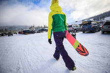Woman Carrying a Snowboard at a Parking Lot of a Ski Resort