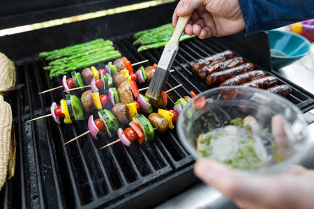 Man braising vegetable skewers on a BBQ grill with a brush
