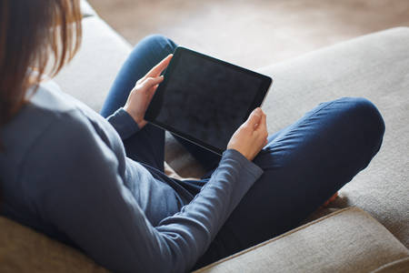 Woman Holding a Digital Tablet Sitting on a Sofa in a Living Room