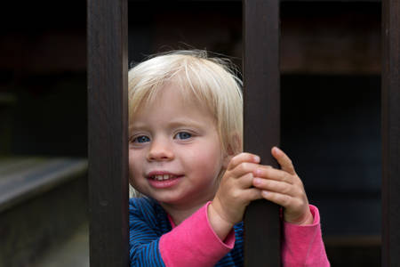 Smiling Toddler Girl Peeking Through a Wooden Fence