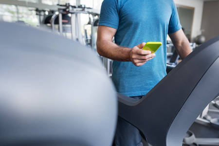 Midsection of a Man with a Cell Phone Standing on Treadmill in a Gym