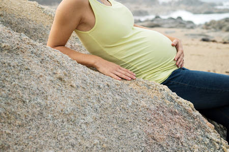 Smiling Pregnant Woman on a Beach Looking at Her Belly