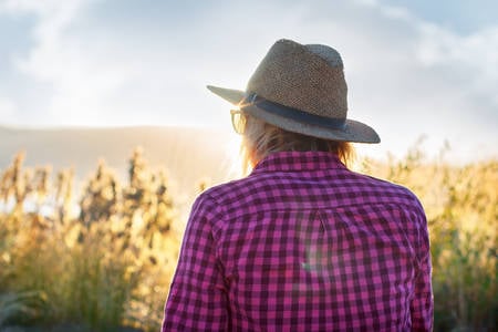 Woman in a Checkered Shirt and a Straw Hat Looking at Sunset