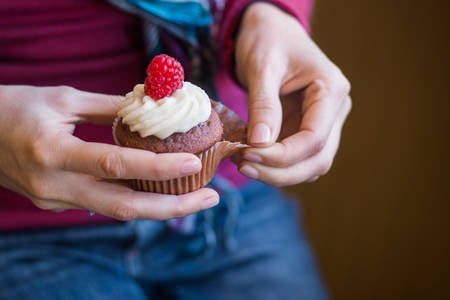 Woman Holding Raspberry Cupcake in Her Hands and Peeling off the Wrapper