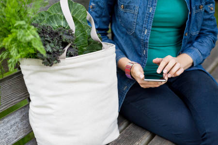 Woman with a Bag of Groceries Sitting on a Bench Holding a Cell Phone