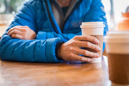 Man in a Coffee Shop Holding a Cup of Coffee in One Hand