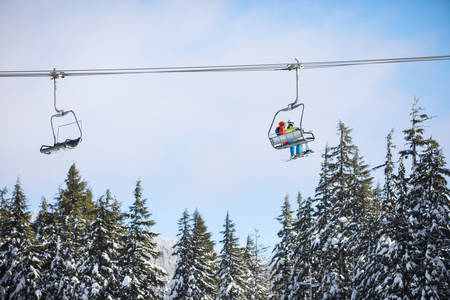 Two Skiers on a Lift Above the Trees Passing a Returning Chair